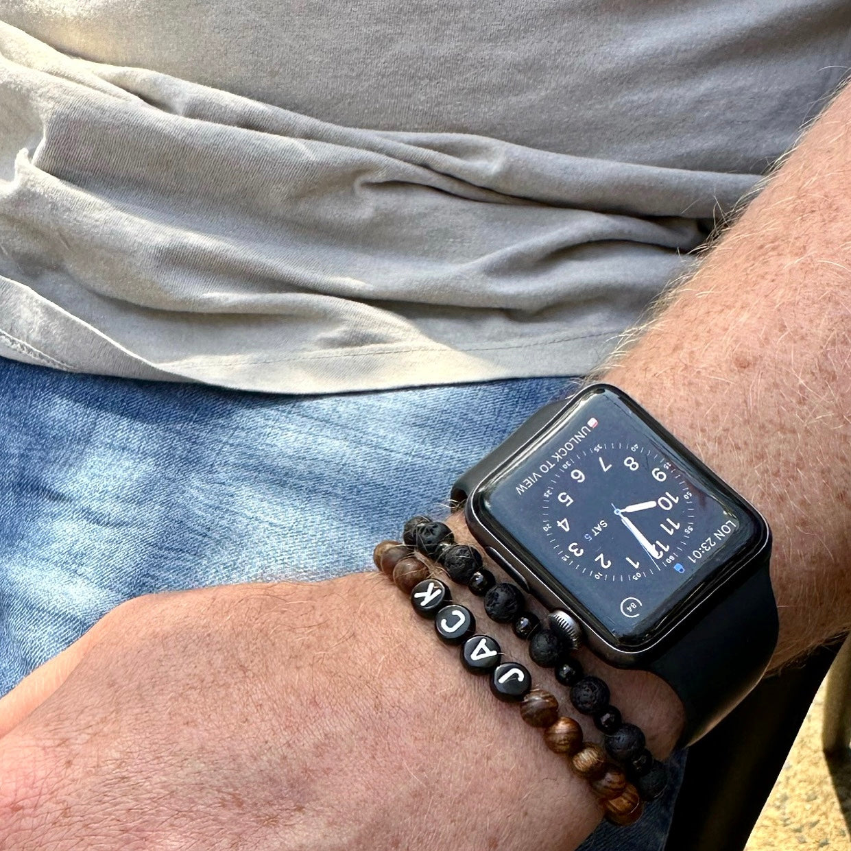 Mans wrist wearing wood bead and lava stone bracelets and watch